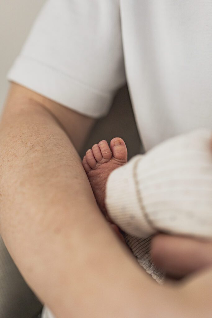Newbornshooting, Babyshooting, Detailfotografie, ein Fuß eines Babys wie es auf dem Arm des Vaters liegt