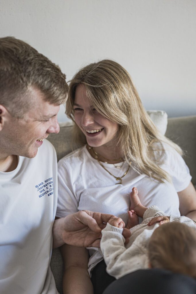 Paarshooting, Newbornshooting, Babyshooting, Baby liegt auf deinen Beinen der Mutter, Vater und Mutter lachen sich an