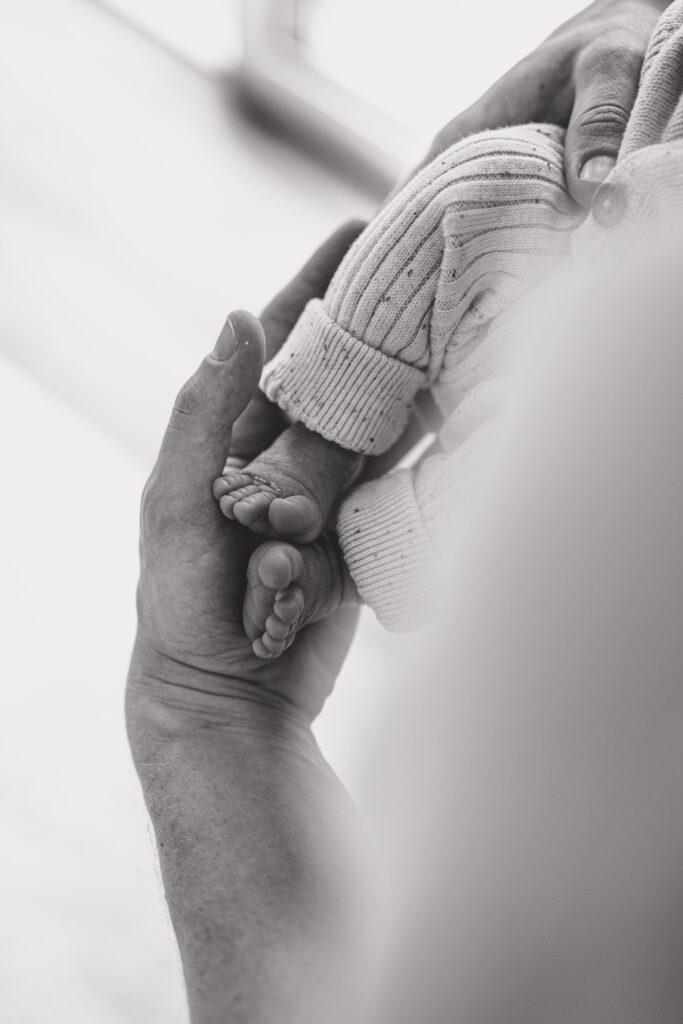 Babyfüße, Newbornshooting, Babyshooting, Baby liegt auf dem Arm des Vaters, die Füße in den Händen